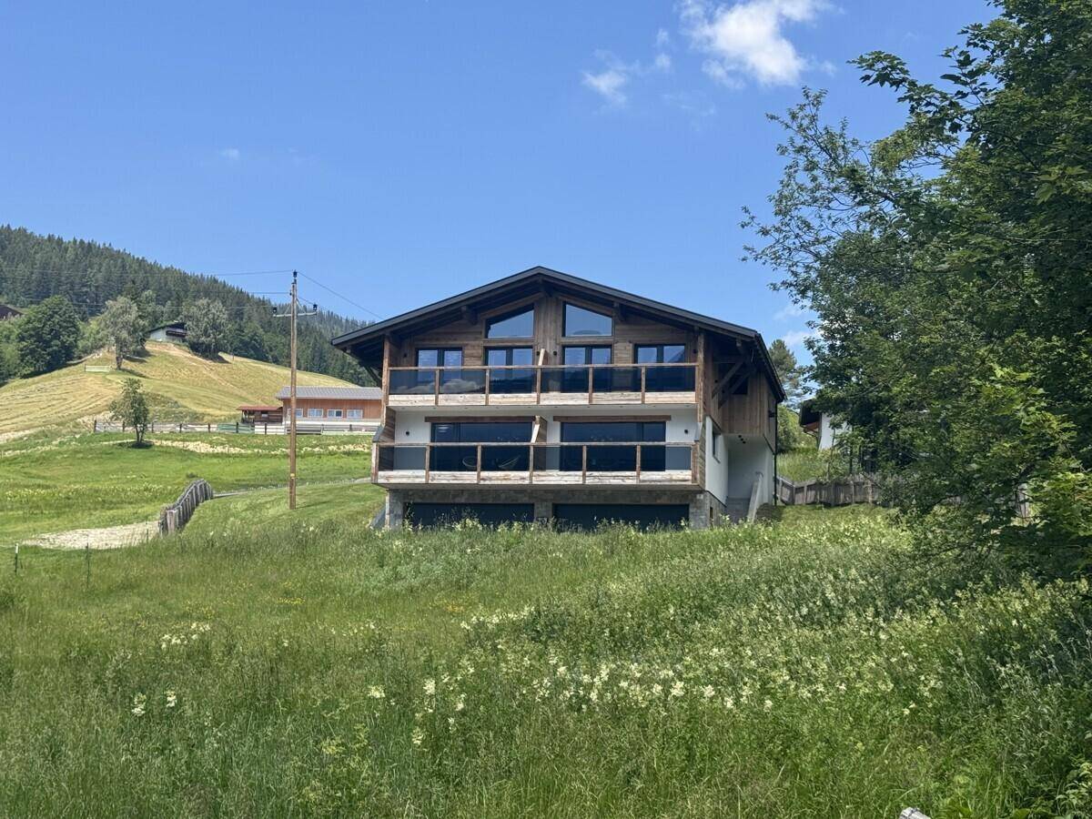 Modernes Holzhaus mit Balkonen und großen Fenstern, eingebettet in eine grüne Berglandschaft.