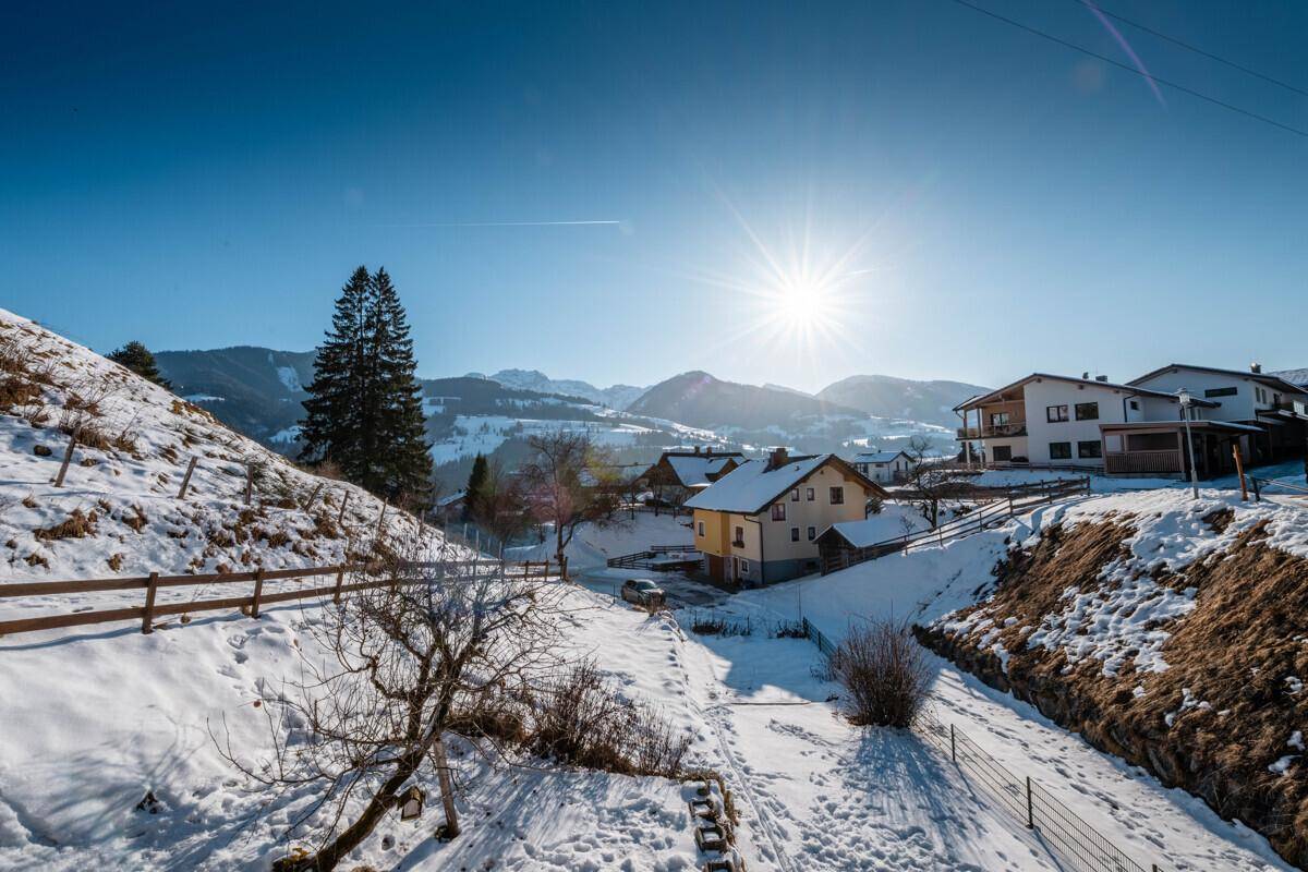 Sonnige Winterlandschaft mit Häusern und Bergen im Hintergrund, weite Aussicht.