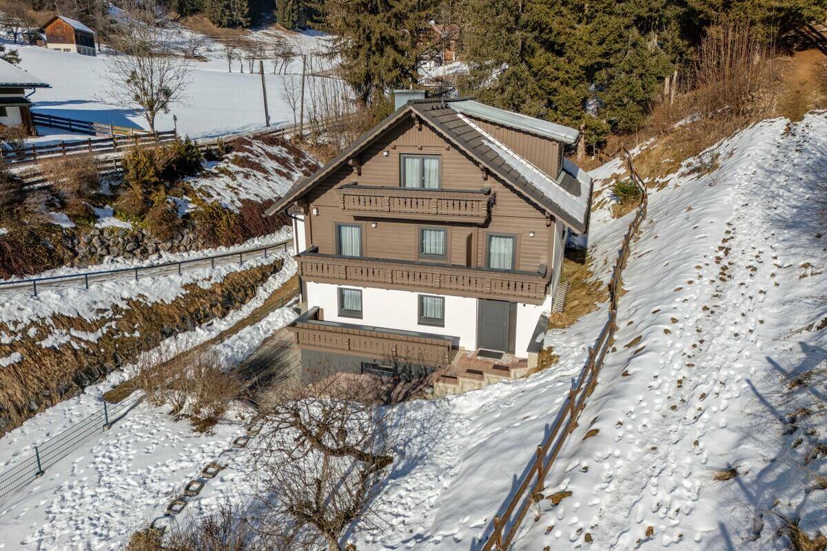 Alpines Wohnhaus mit brauner Holzfassade und Balkonen, eingebettet in verschneite Natur.