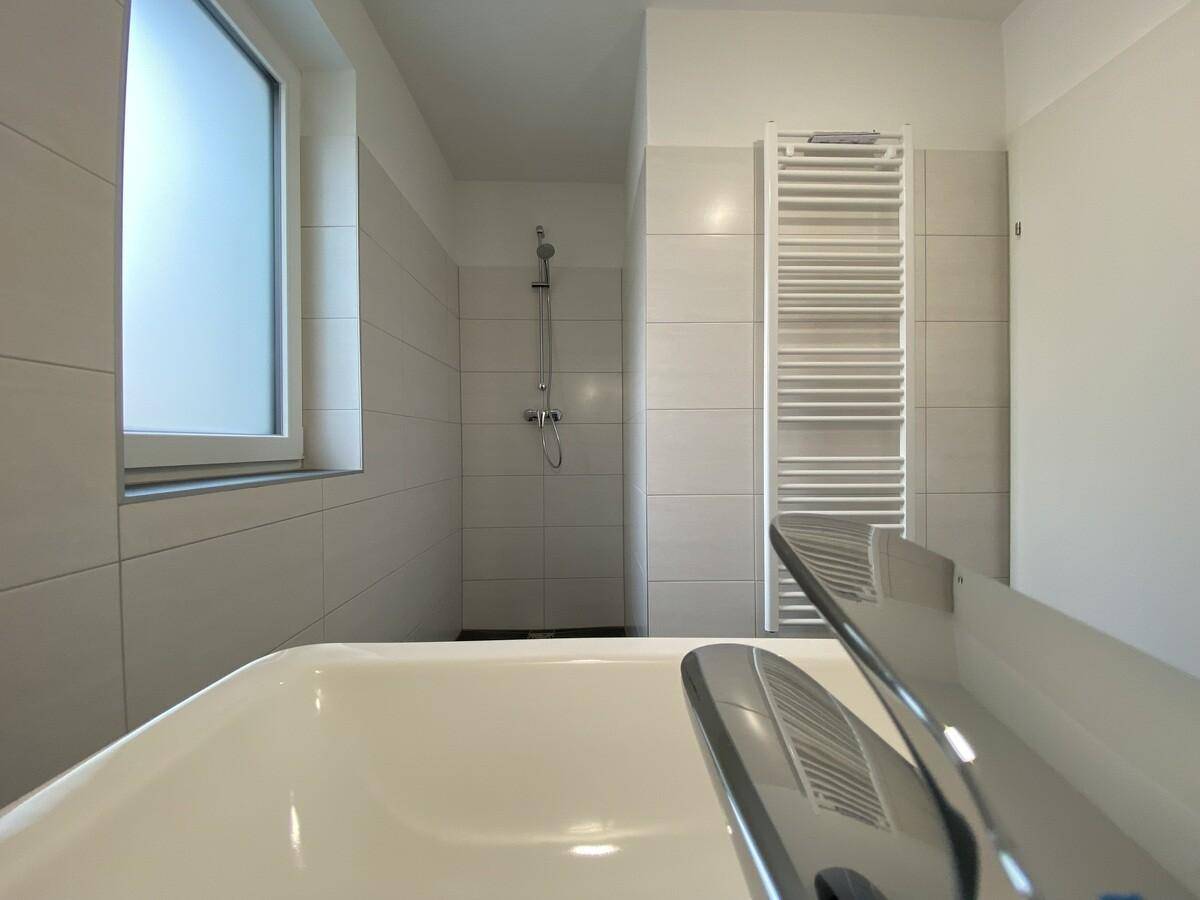Helles Badezimmer mit Dusche, Badewanne, beheiztem Handtuchhalter und Fenster.