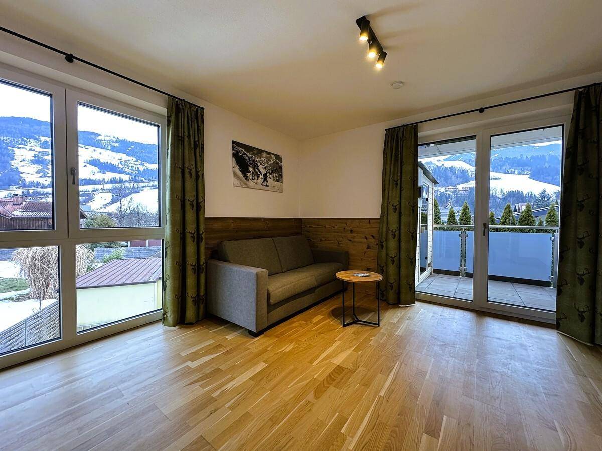 Helles Wohnzimmer mit Sofa, Holzboden und großen Fenstern mit Blick auf die Berge.