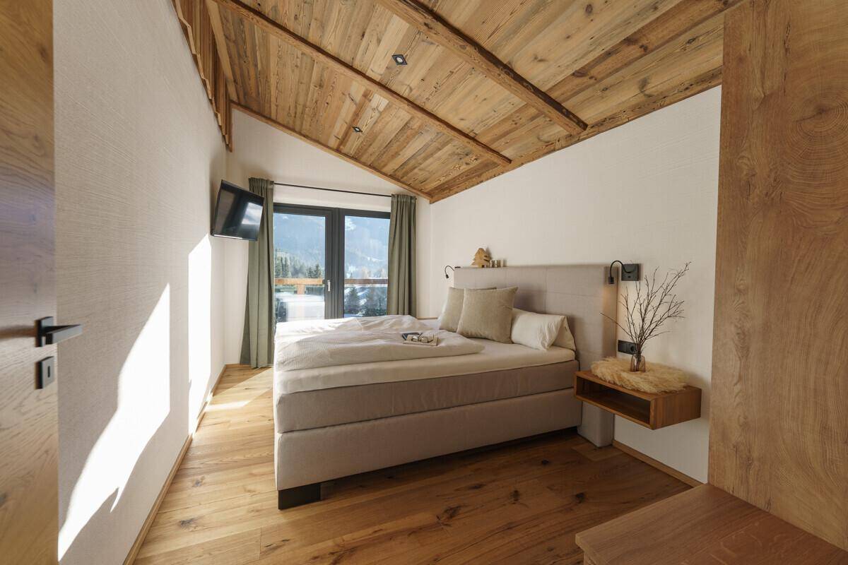Helles Schlafzimmer mit Doppelbett, Holzboden und einer charmanten Holzdecke mit Dachschräge.