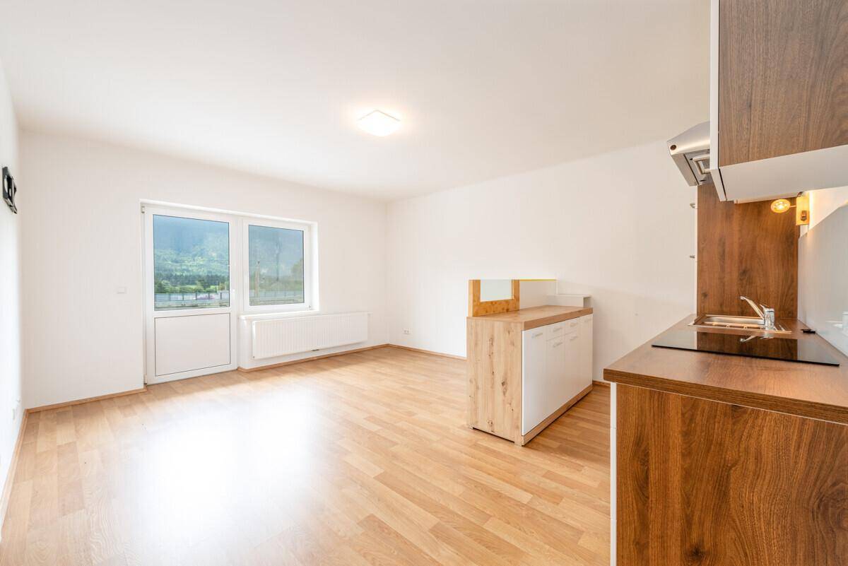 Heller Wohnbereich mit kleiner Küchenzeile, Laminatboden und Zugang zum Balkon.