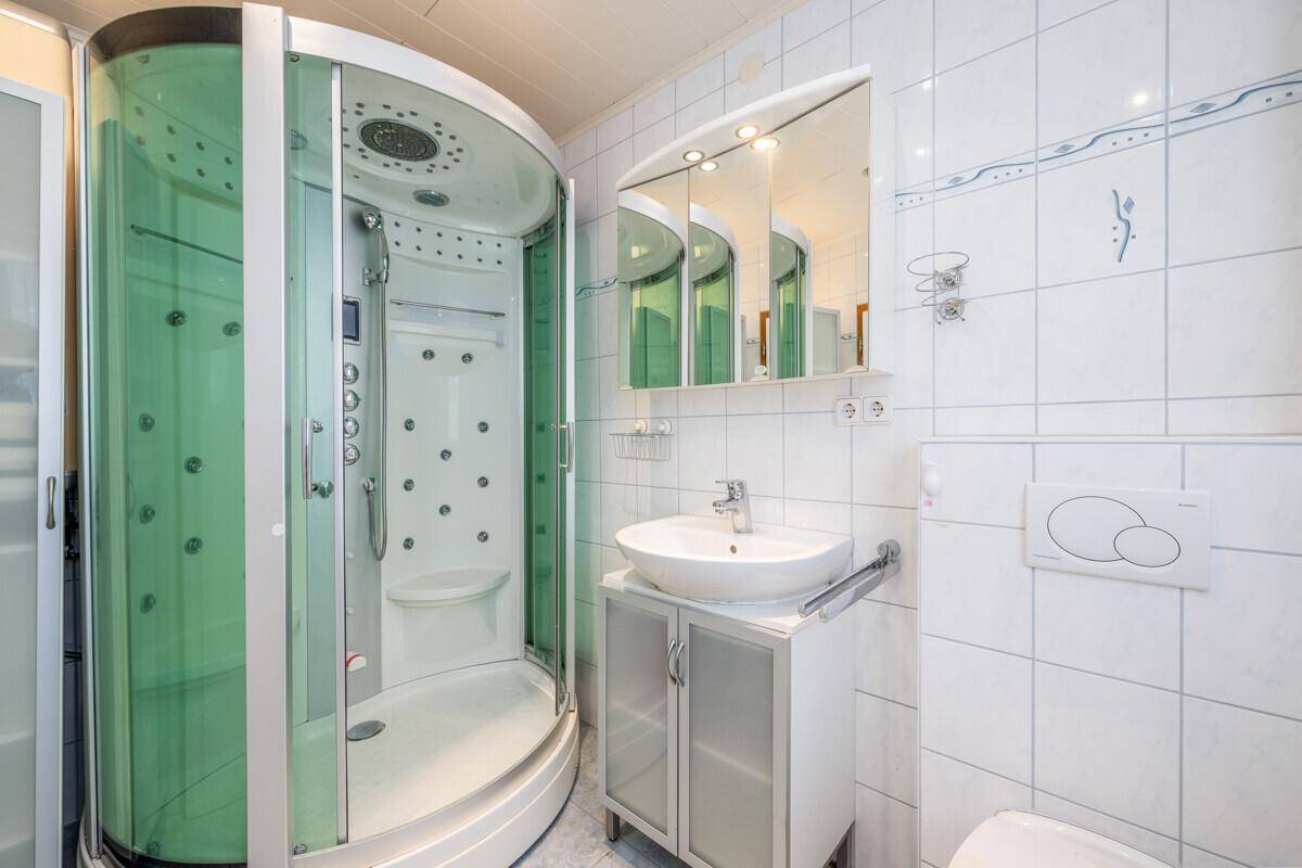 Modernes Badezimmer mit Duschkabine, Waschbecken und Spiegelschrank, hell gefliest.