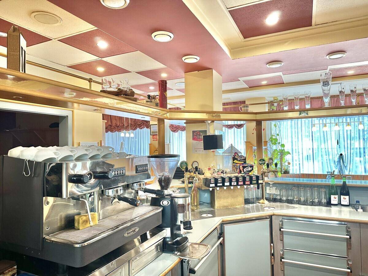 Professionelle Bar mit Espressomaschine, Zapfanlage und vielen Gläsern unter einer karierten Decke.