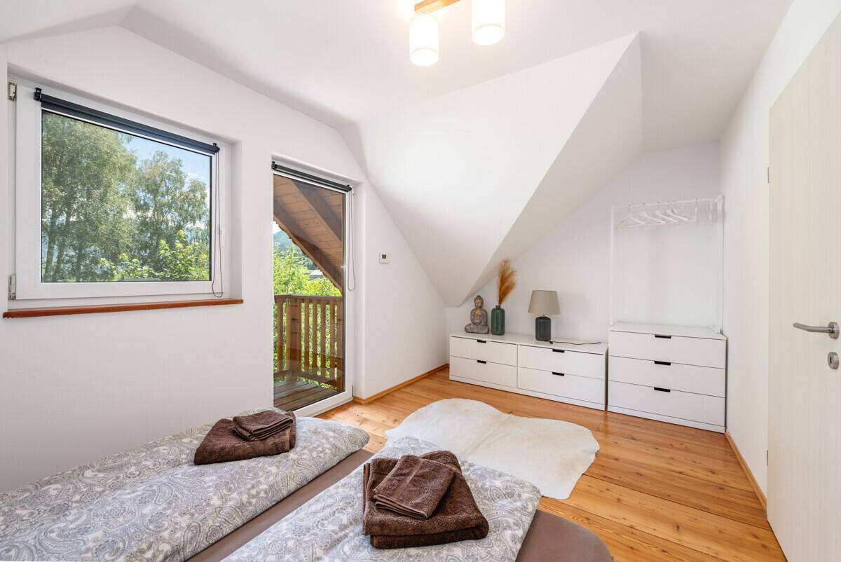 Schlafzimmer mit Doppelbett, Kommode, Holzboden und Zugang zum Balkon.