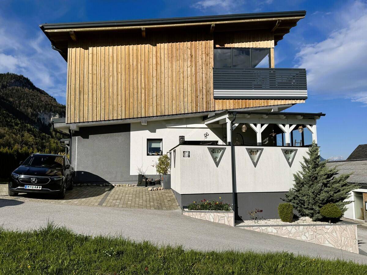 Modernes Wohnhaus mit Holzfassade, Balkon und gepflasterter Auffahrt.