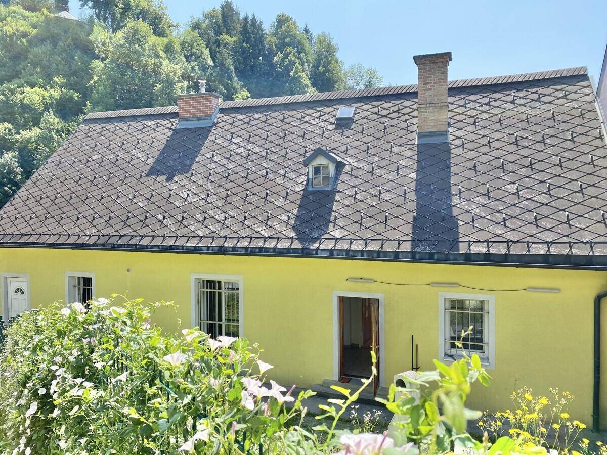 Gelbes Haus mit Satteldach und grüner Umgebung an einem sonnigen Sommertag.