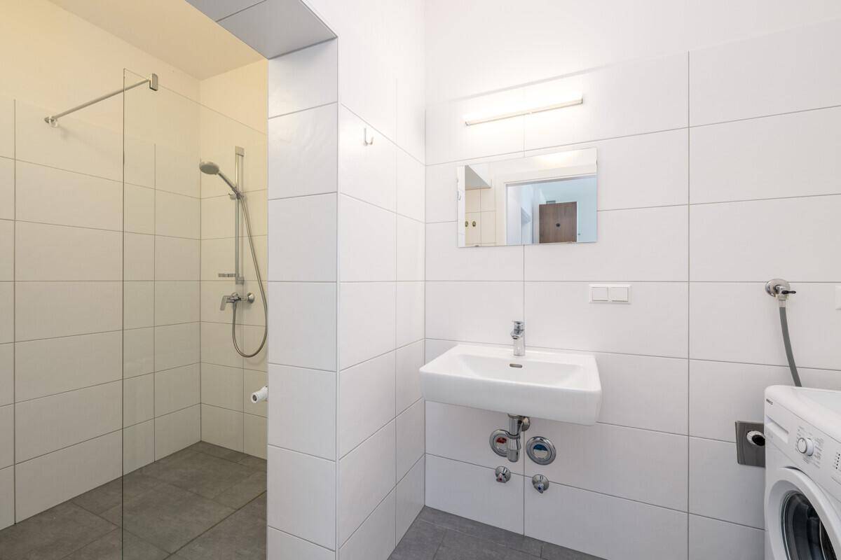 Modernes Badezimmer mit Dusche, Waschbecken und Waschmaschine, komplett gefliest.