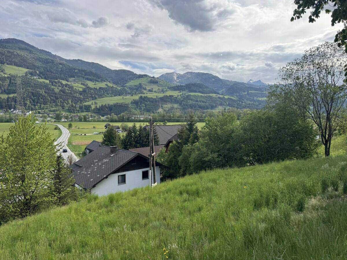 Haus eingebettet in eine grüne Hügellandschaft mit weitem Blick auf die Berge.