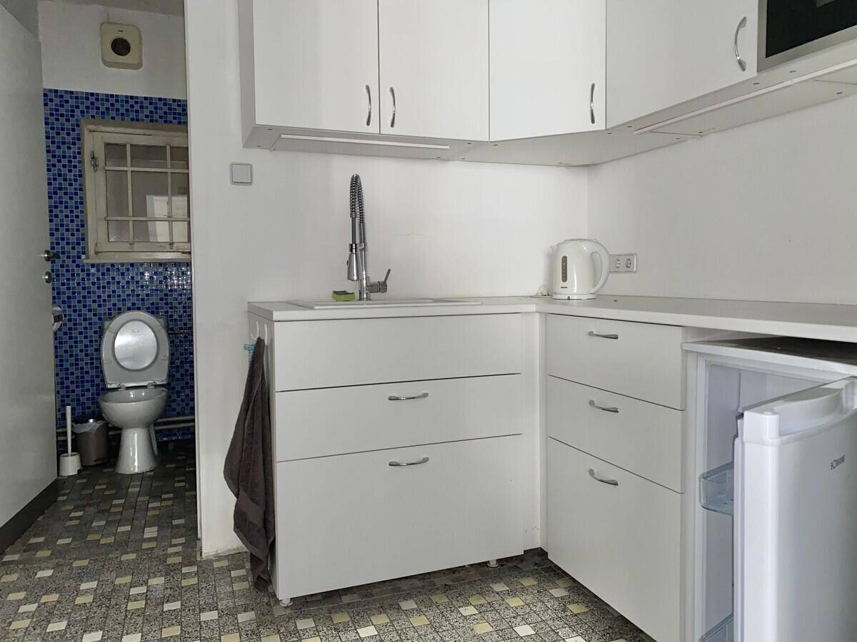 Kleine Küchenzeile mit weißen Schränken und angrenzendem Toilettenbereich mit blauen Mosaikfliesen.