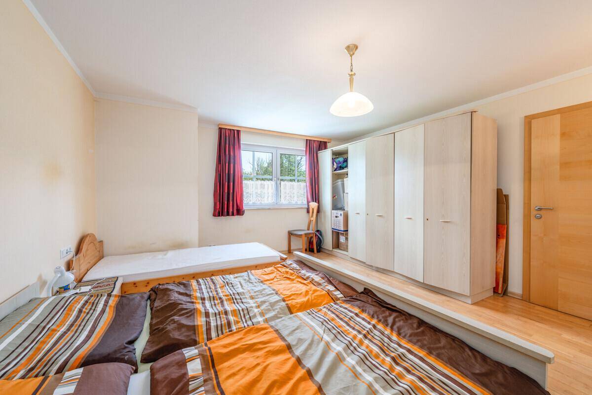 Schlafzimmer mit mehreren Betten, hellem Holzschrank und Fenster mit rotem Vorhang.