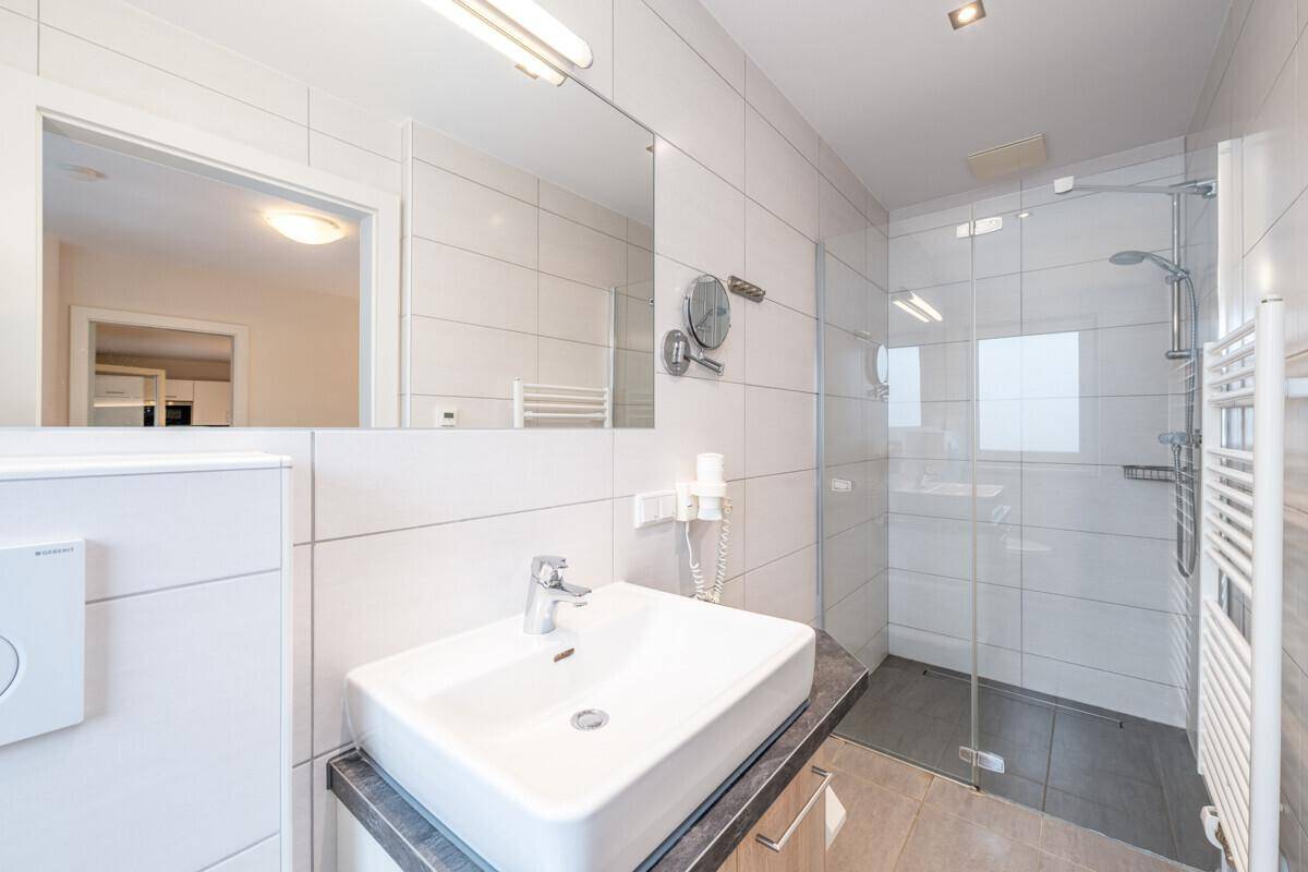 Modernes Badezimmer mit Einzelwaschbecken, großem Spiegel und begehbarer Dusche.