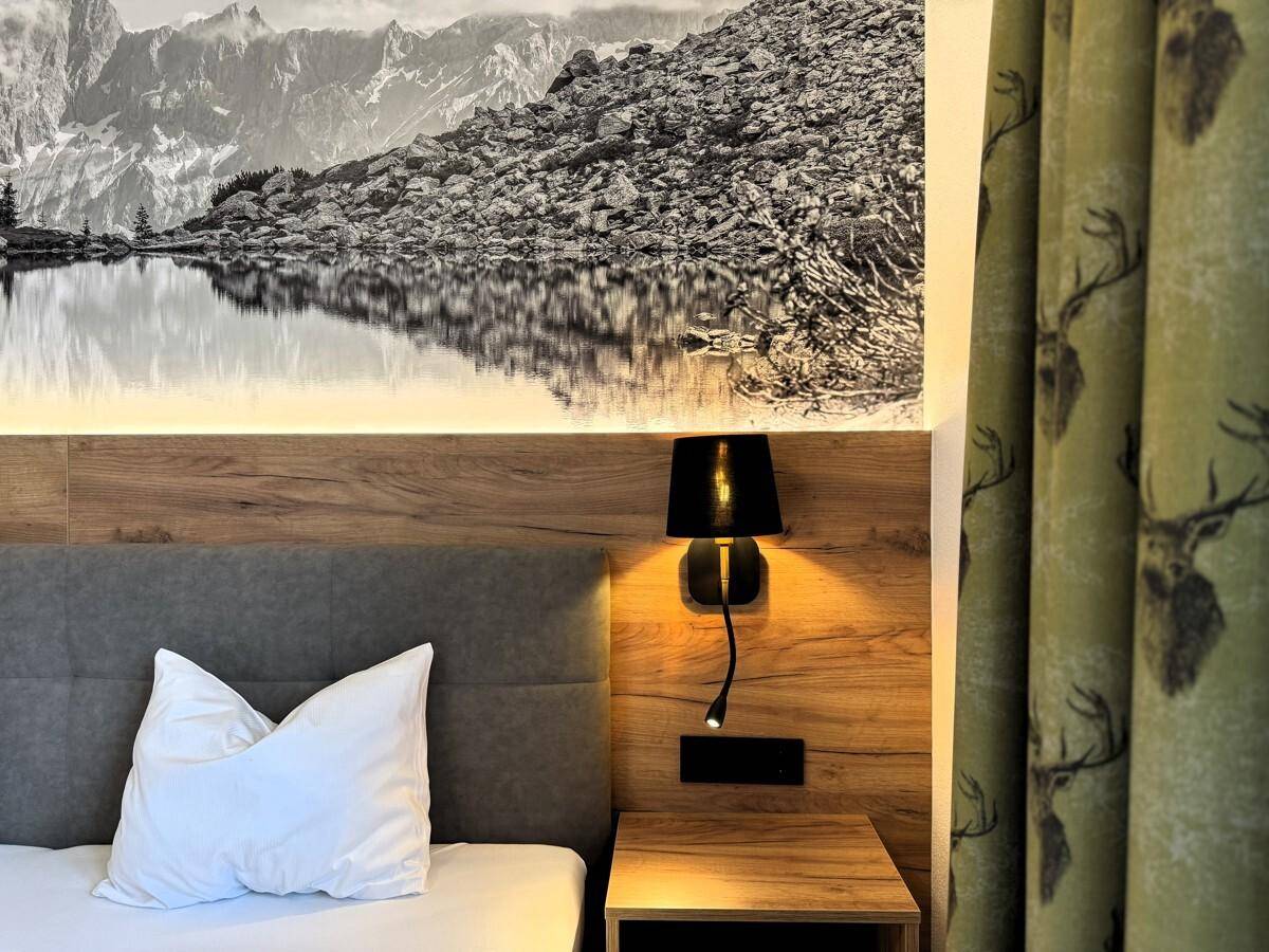 Nahaufnahme des Bettes mit Kissen und des Vorhangs mit Hirschmotiv im Schlafzimmer.