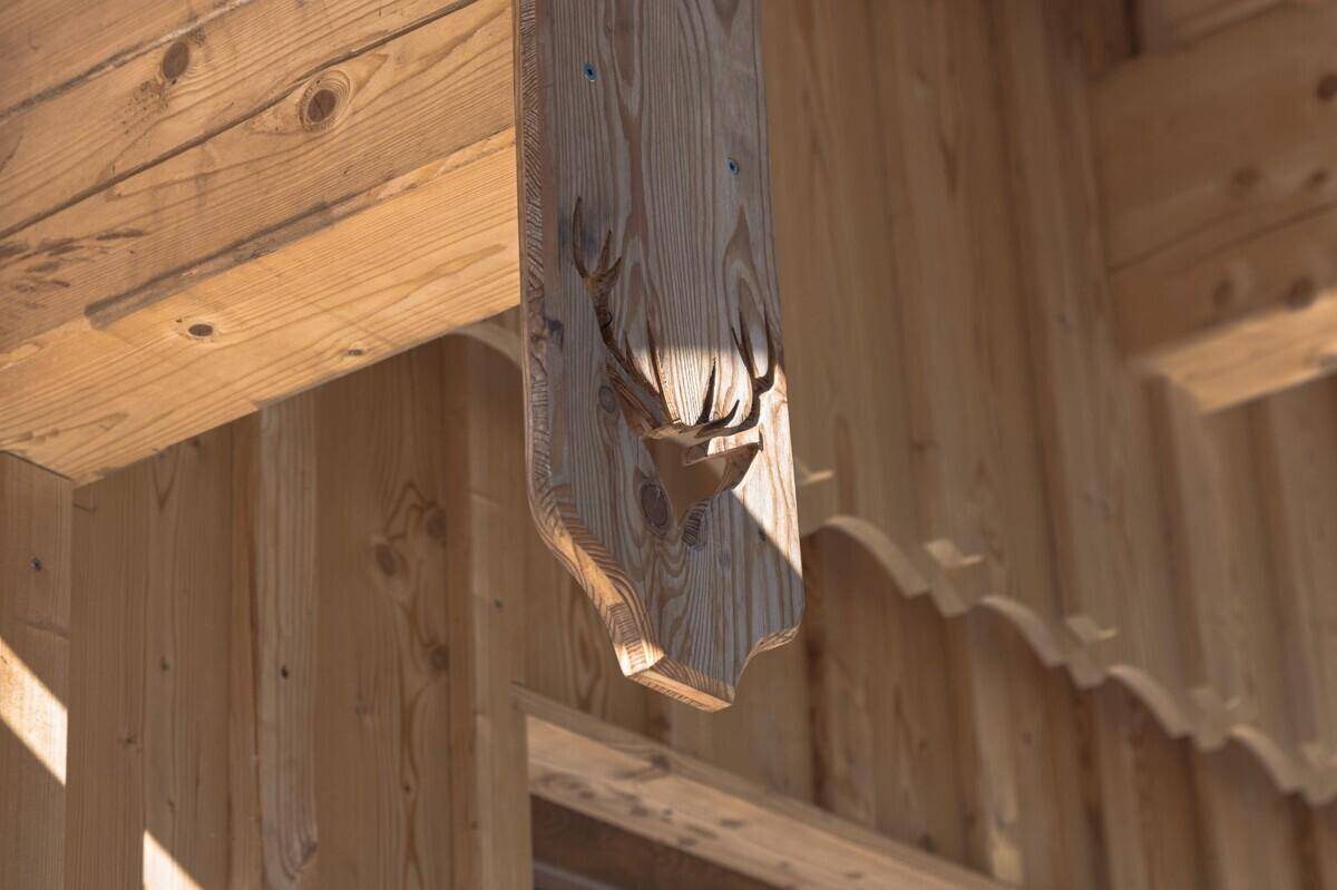 Detailansicht einer geschnitzten Hirschkopf-Dekoration aus Holz an der Fassade eines Alpenhauses.