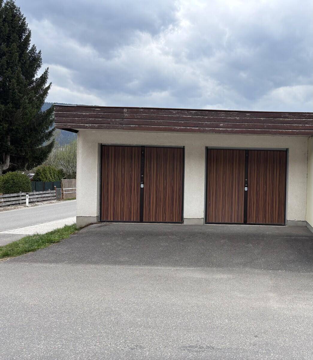 Zwei Garagentore aus Holz mit dunklen Rahmen an einem Gebäude mit heller Fassade.