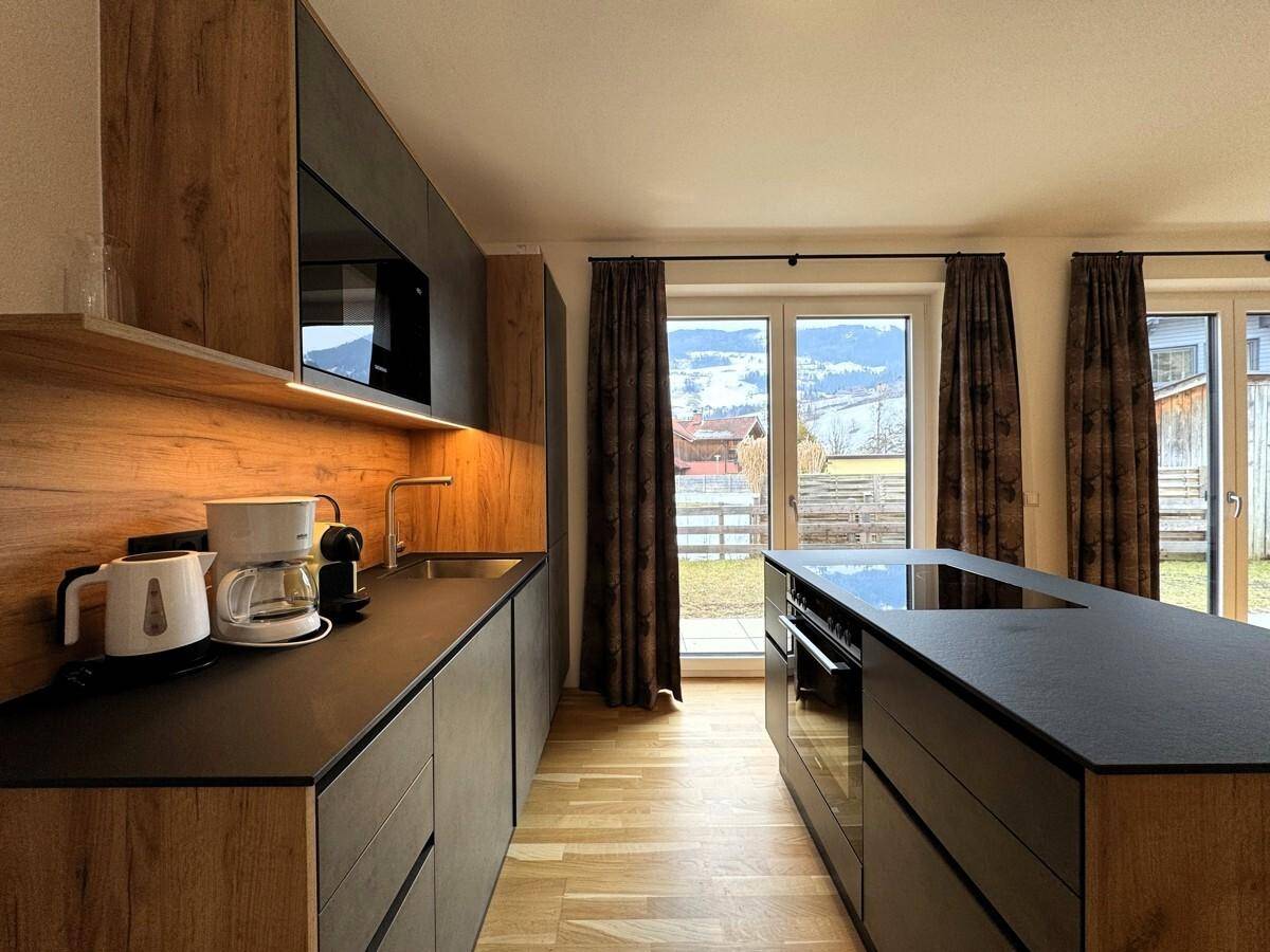 Moderne Küche mit dunklen Fronten, Holzakzenten und integriertem Backofen, mit Blick auf die Berge.