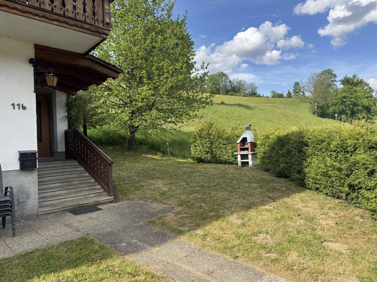 Gartenbereich vor dem Haus mit Rasenfläche, Hecke und einem gemauerten Grillplatz.