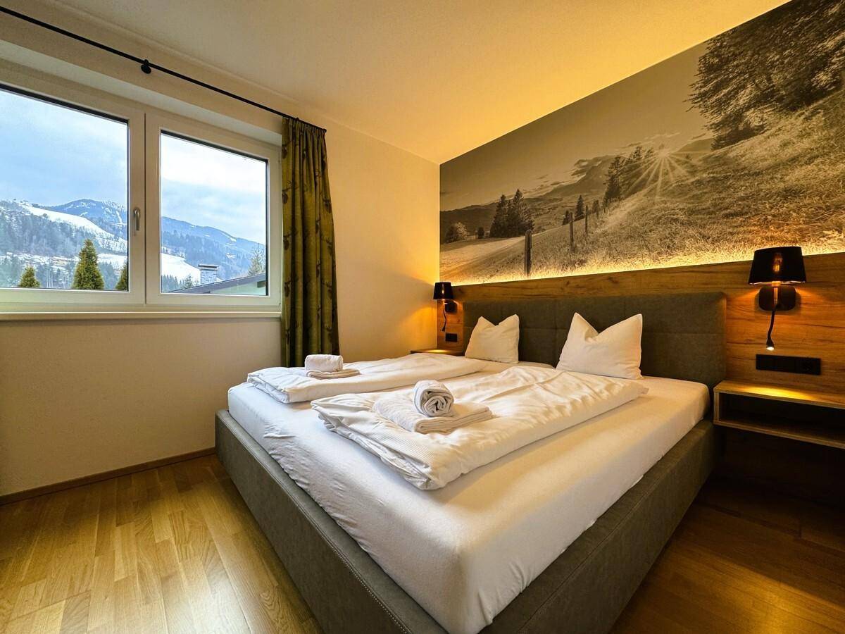 Gemütliches Schlafzimmer mit Doppelbett, Holzboden und Blick auf die verschneiten Berge.