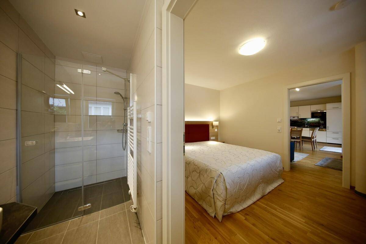 Schlafzimmer mit direktem Zugang zu einem modernen Badezimmer mit begehbarer Dusche und Fliesenboden.