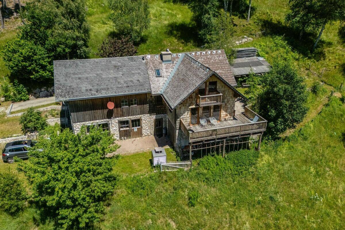 Luftaufnahme des Chalets mit großer Holzterrasse, umgeben von üppiger grüner Natur und Wald.