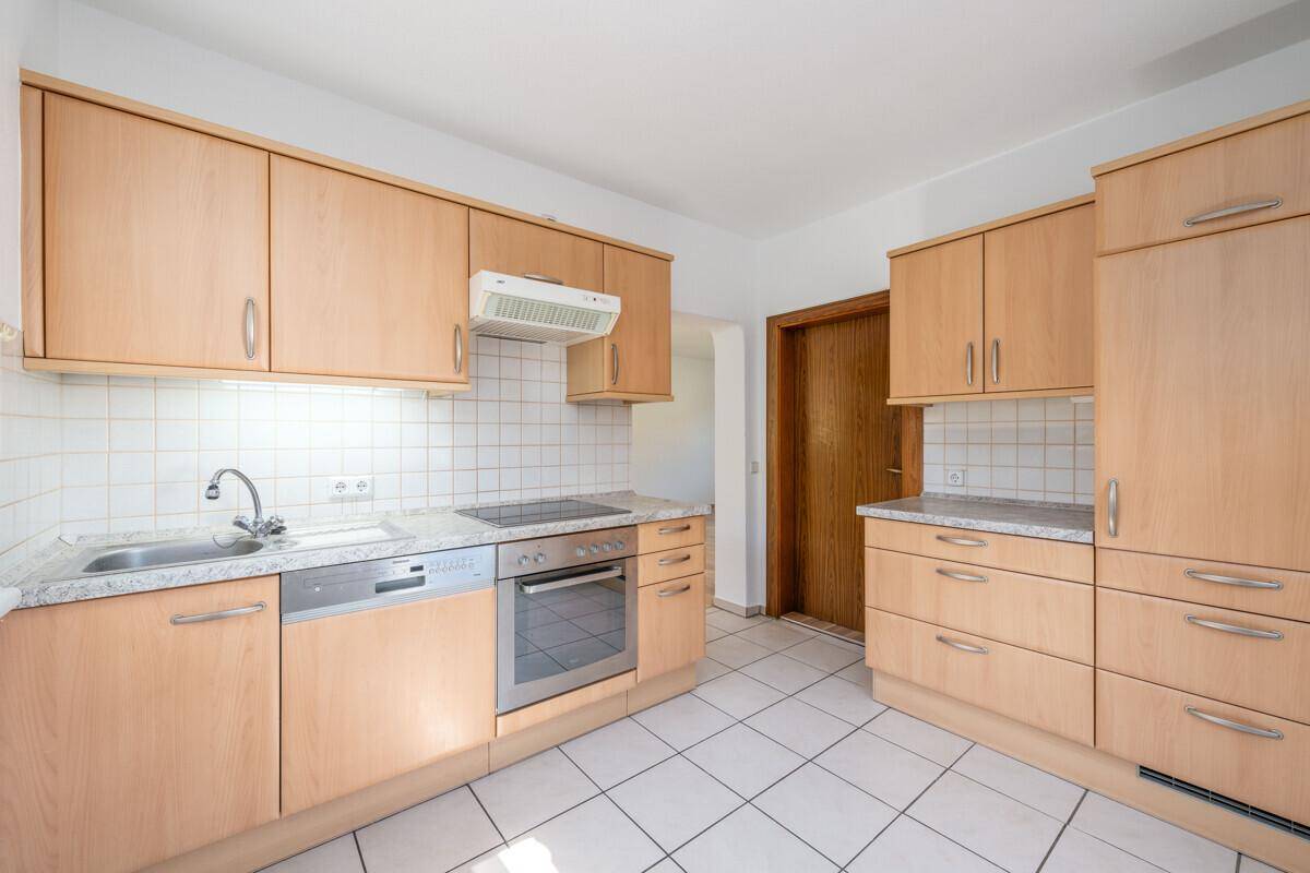 Funktionale Küche mit hellen Holzschränken, Fliesenboden und integrierten Geräten.