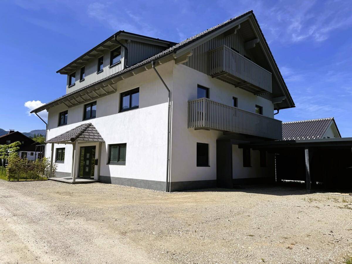 Modernes Einfamilienhaus mit weißer Fassade, Holzbalkonen und Carport unter blauem Himmel.