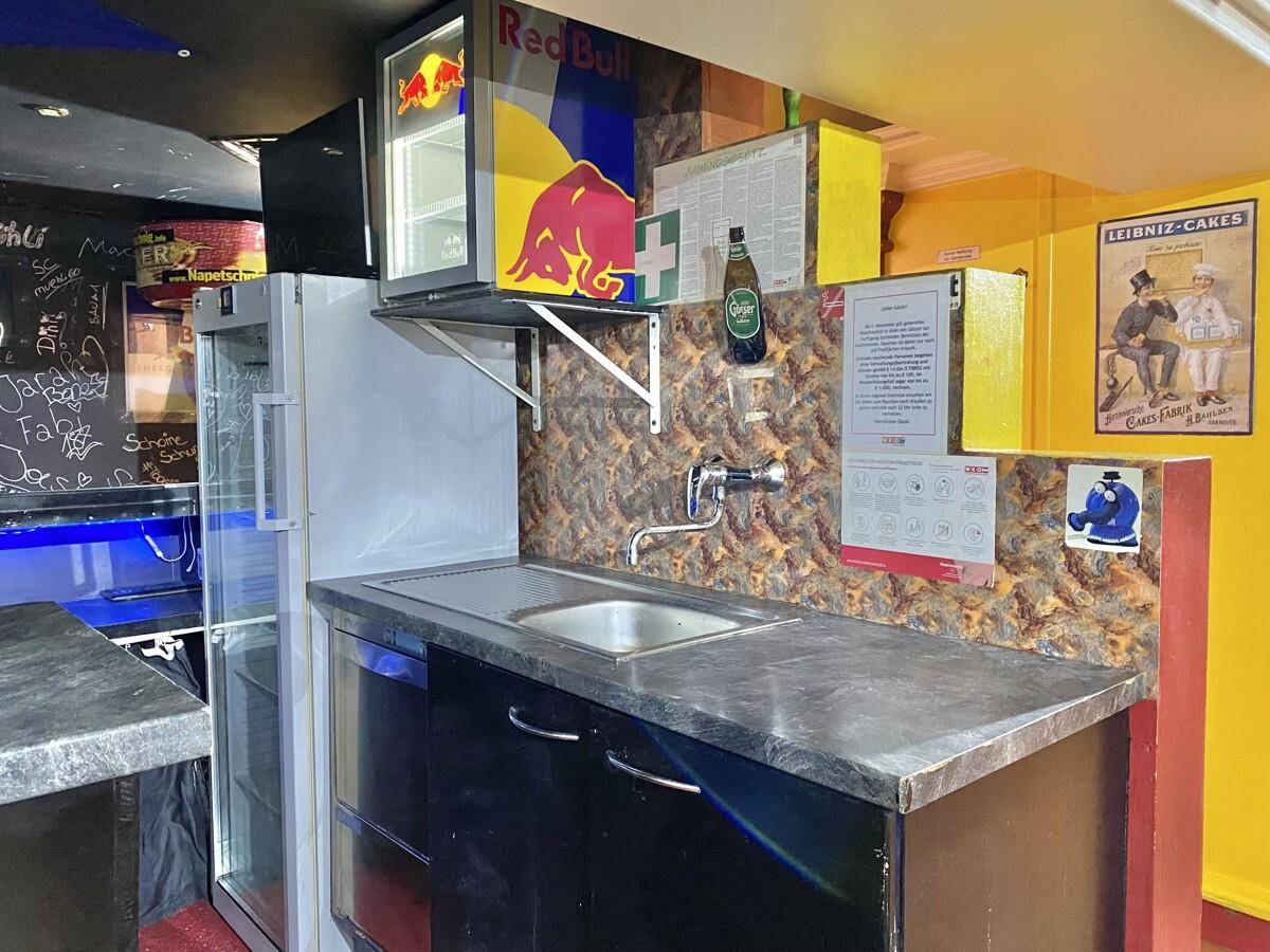 Kleiner Servicebereich hinter der Bar mit Spülbecken, Arbeitsplatte und einem Red Bull Kühlschrank.