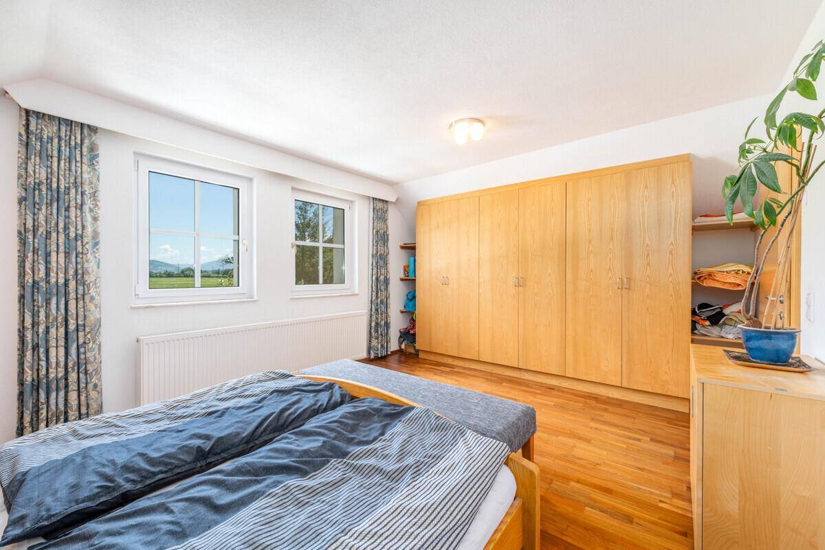 Helles Schlafzimmer mit Holzboden, Einbauschränken und Fenstern mit Blick auf die Landschaft.