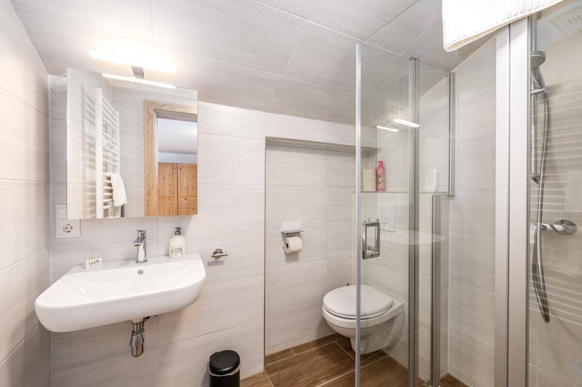 Funktionales Badezimmer mit Dusche, Waschbecken und Spiegel, hell gefliest.