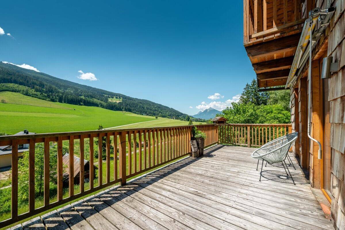 Großer Holzbalkon mit Sitzgelegenheiten und weitem Panoramablick auf die grüne Berglandschaft.