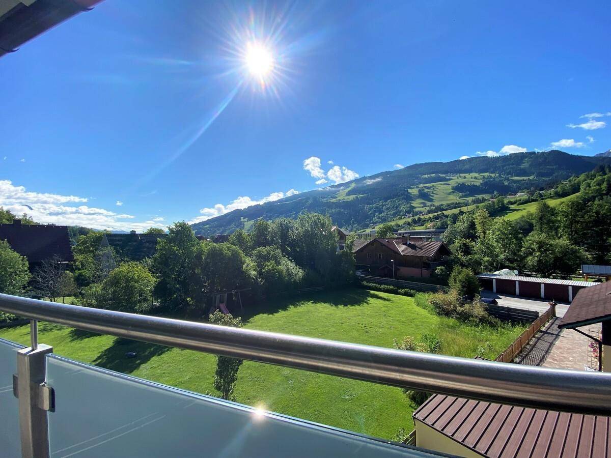 Sonniger Balkon mit Glasgeländer und atemberaubendem Blick auf die grüne Landschaft.