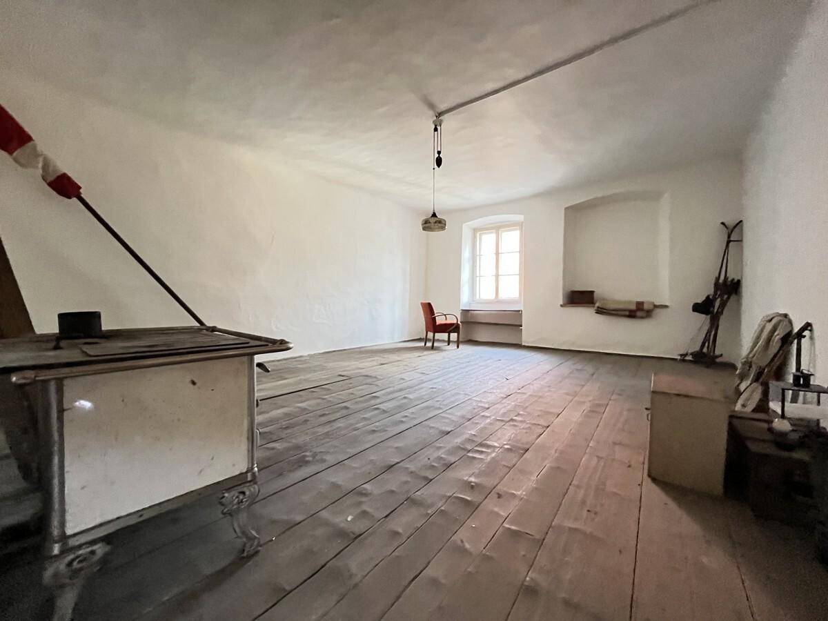 Geräumiger, leerer Raum mit Holzdielenboden und einem alten Ofen, der auf eine frühere Nutzung hinweist.