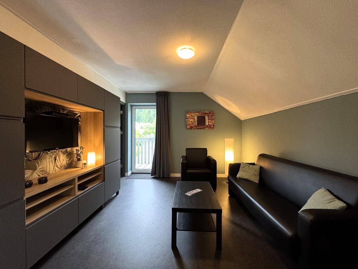 Gemütliches Wohnzimmer mit Ledersofa, Medieneinheit und Balkonzugang.
