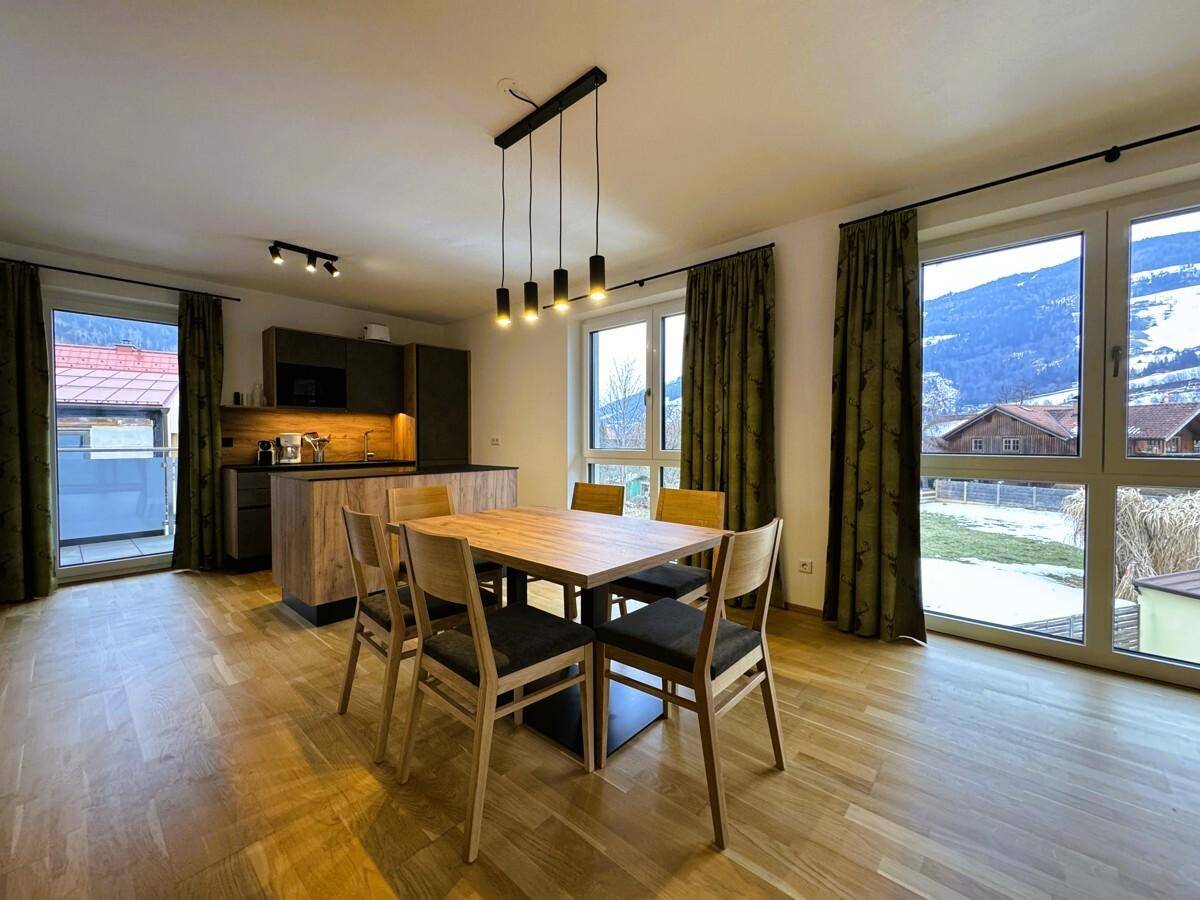 Heller Wohn-Essbereich mit offener Küche, Holzboden und großen Fenstern mit Bergblick.