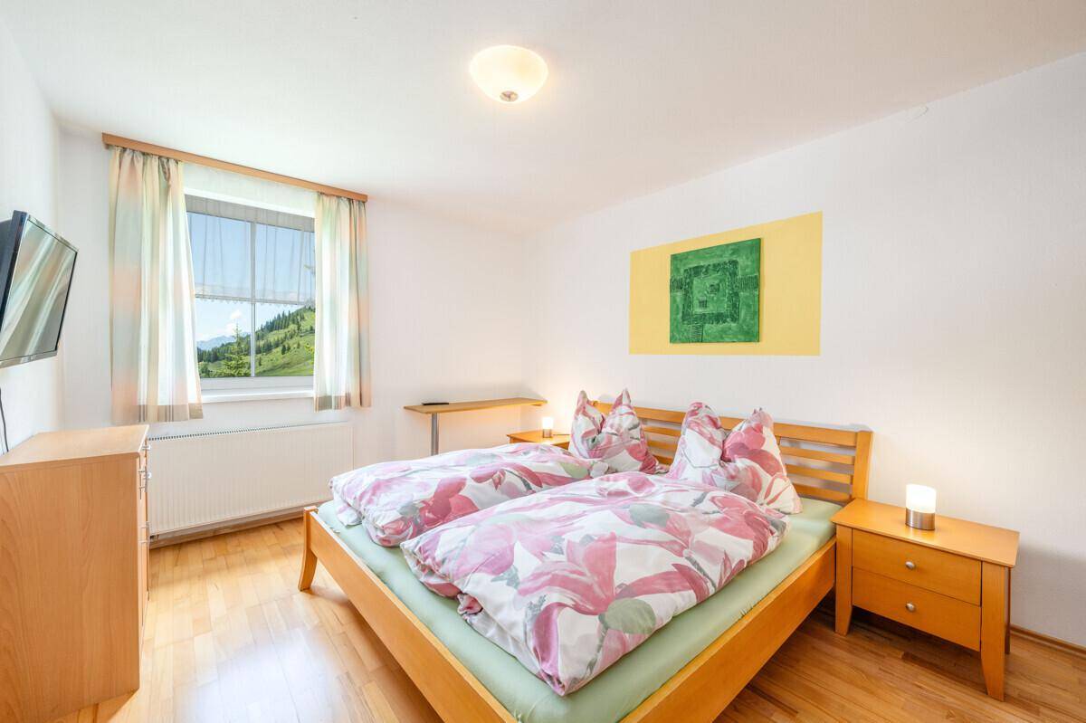 Schlafzimmer mit Doppelbett, Holzmöbeln und einem Fenster, das einen schönen Blick ins Grüne bietet.