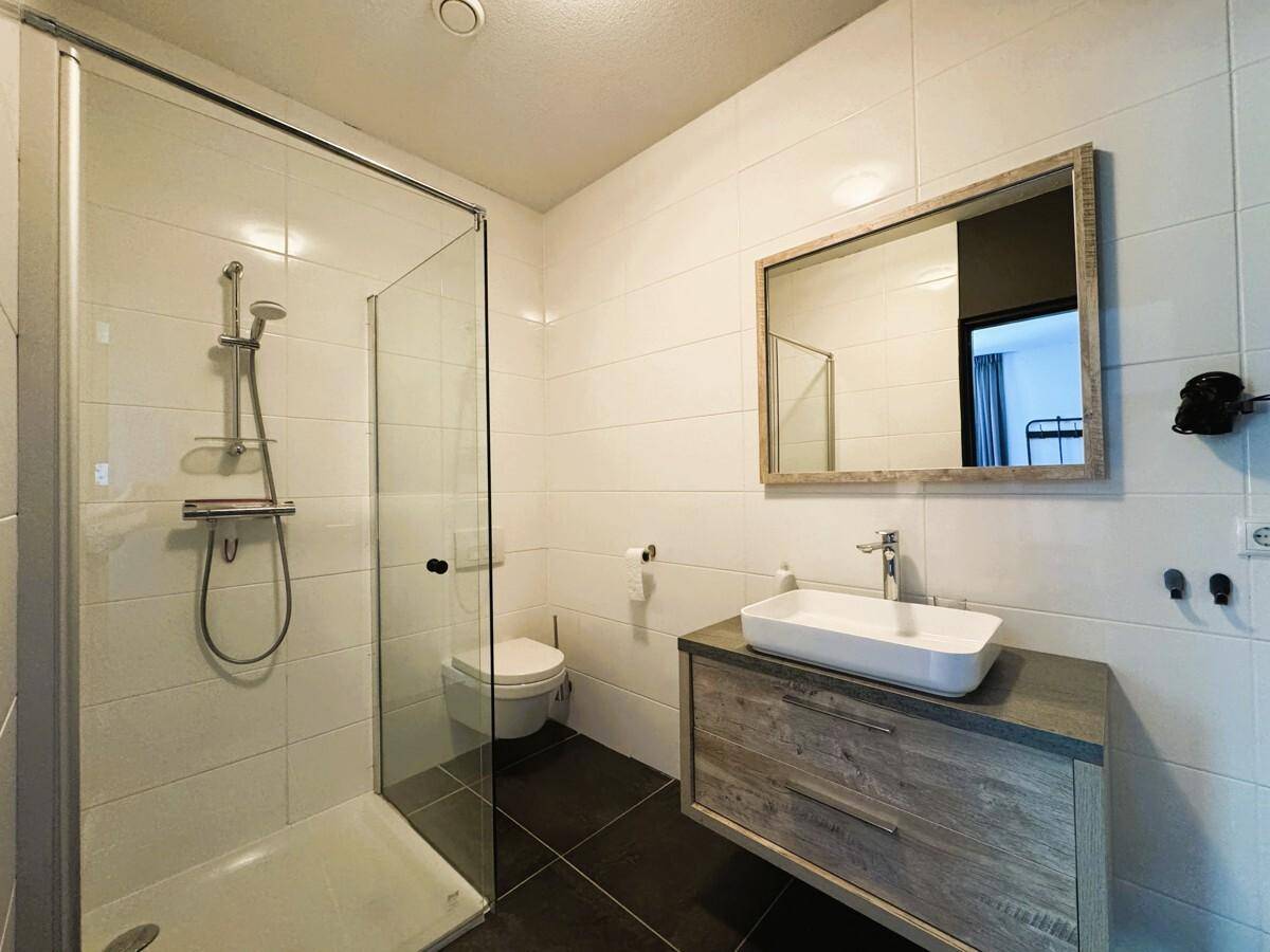 Helles Badezimmer mit Dusche, Waschtisch und Spiegel, modern gefliest.