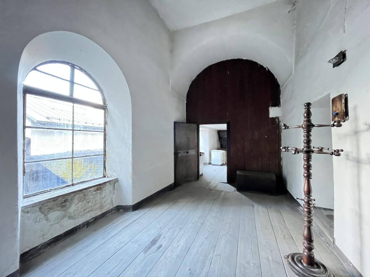 Heller Raum mit einem großen Rundbogenfenster, Holzdielenboden und einer Holzwand im Hintergrund.