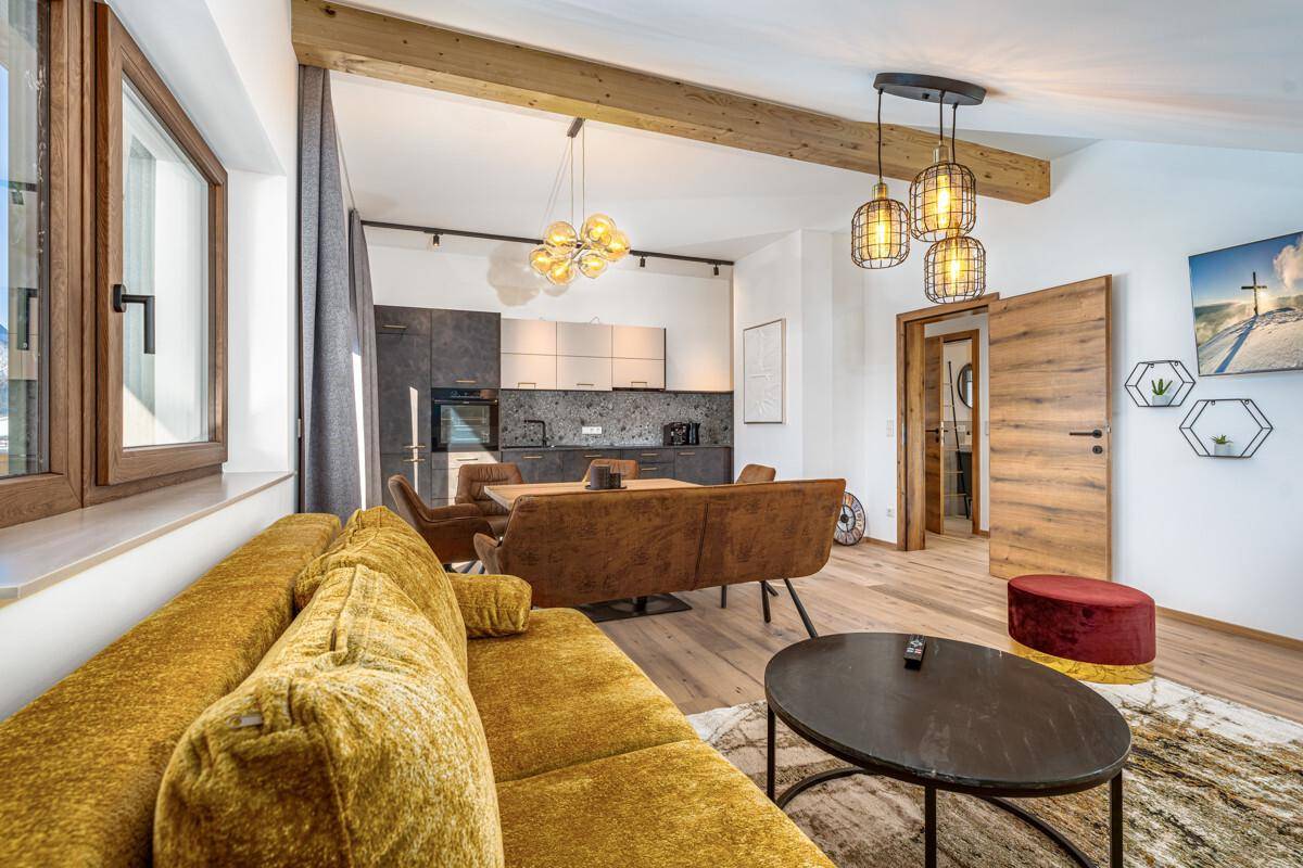 Offener Wohn- und Essbereich mit moderner Küche, Holzbalken und gemütlichem Sofa.