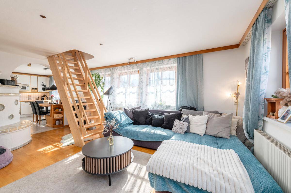 Geräumiges Wohnzimmer mit bequemer Couch, Holztreppe und offenem Übergang zum Essbereich.