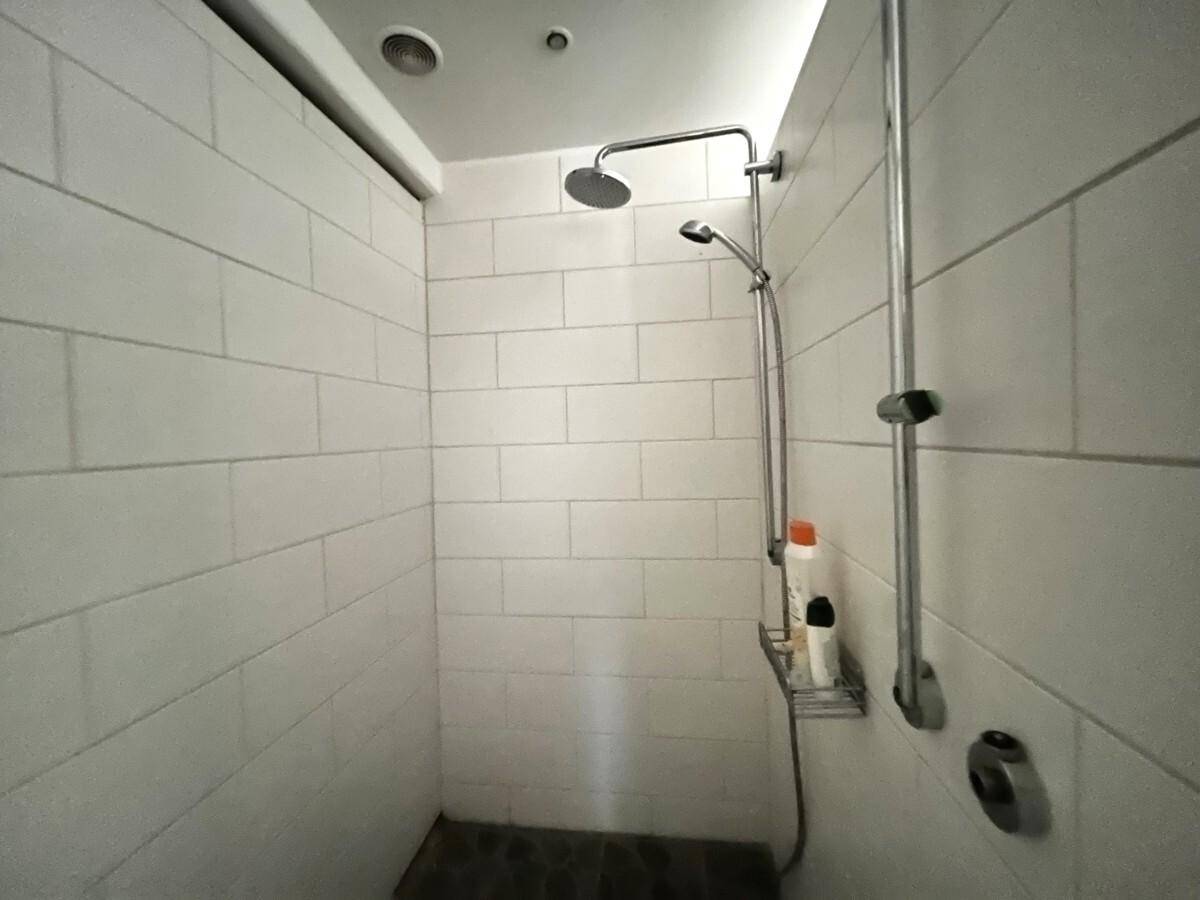 Moderne Duschkabine mit weißen Fliesen und Regenduschkopf in einem renovierten Bad.