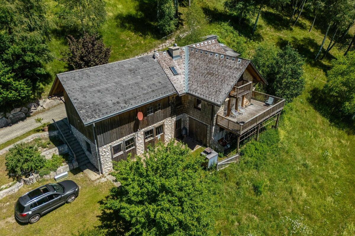 Das rustikale Chalet mit Steinsockel und Holzfassade liegt inmitten einer sonnigen, grünen Landschaft.