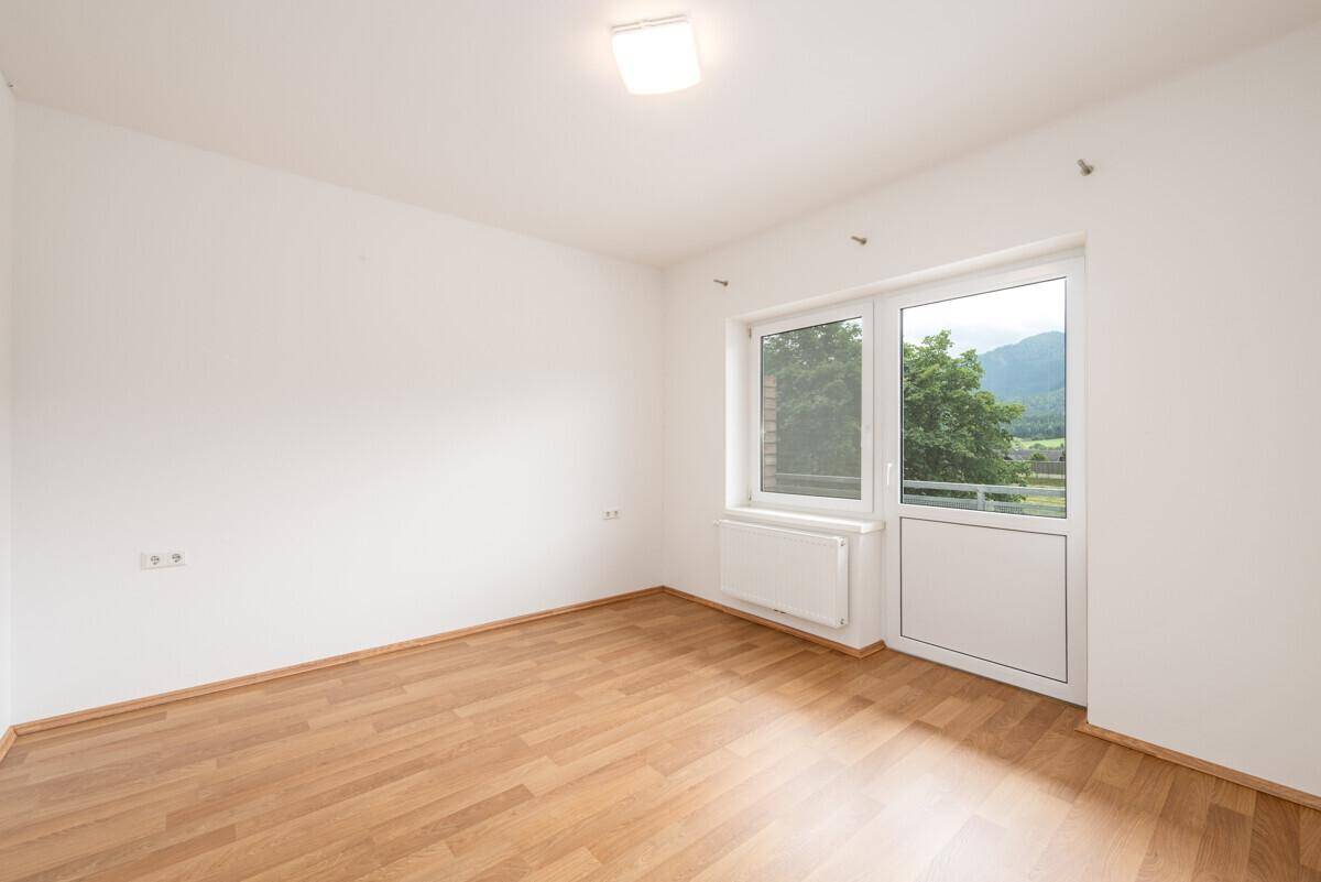 Helles Zimmer mit Laminatboden, weiß gestrichenen Wänden und Fenster mit Bergblick.