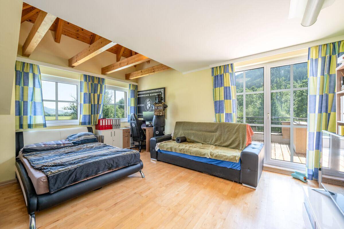 Helles Schlafzimmer mit Holzboden, Balkonzugang und Blick auf die grüne Umgebung.