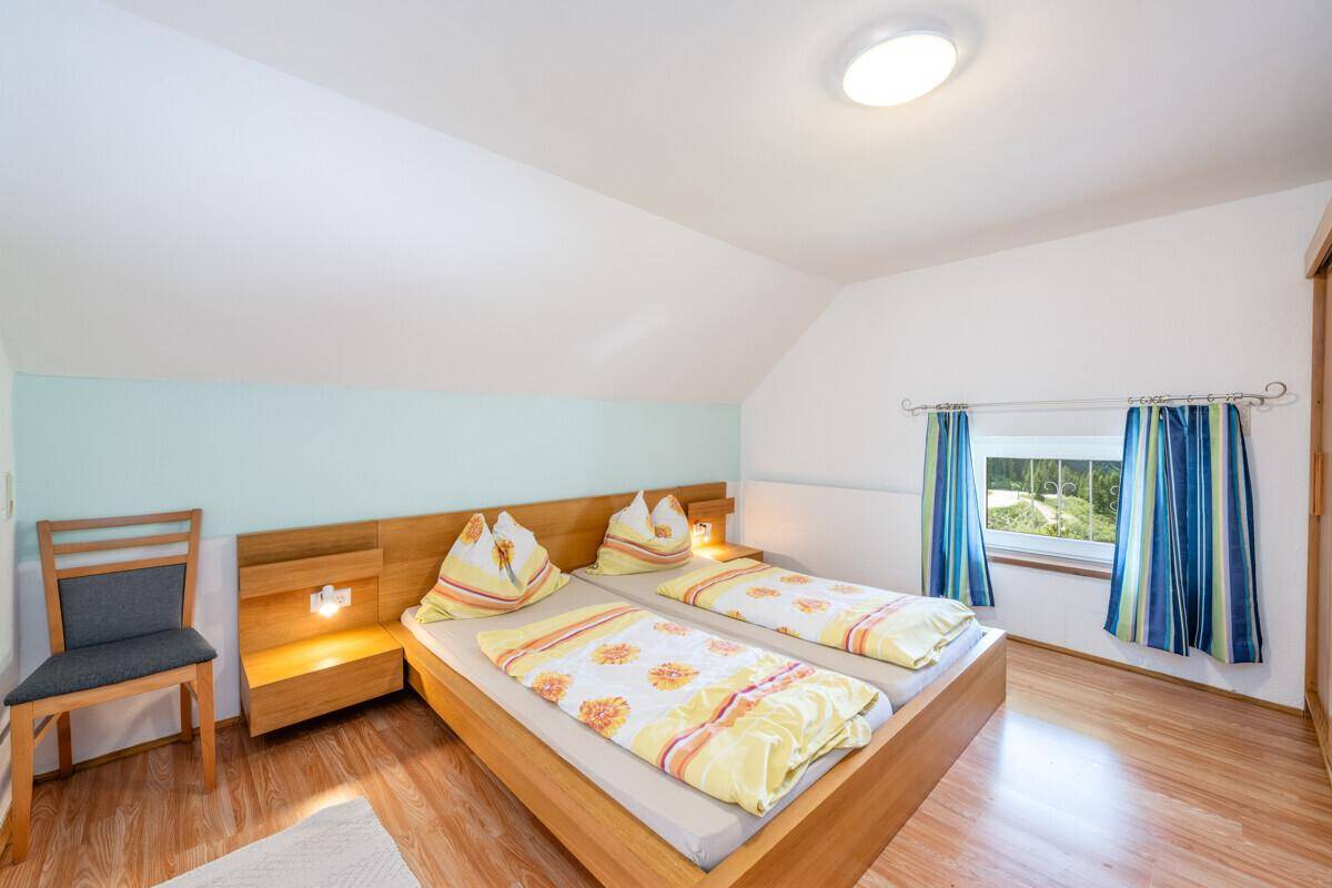 Schlafzimmer mit Doppelbett, Holzmöbeln und einer Dachschräge, die Gemütlichkeit verleiht.
