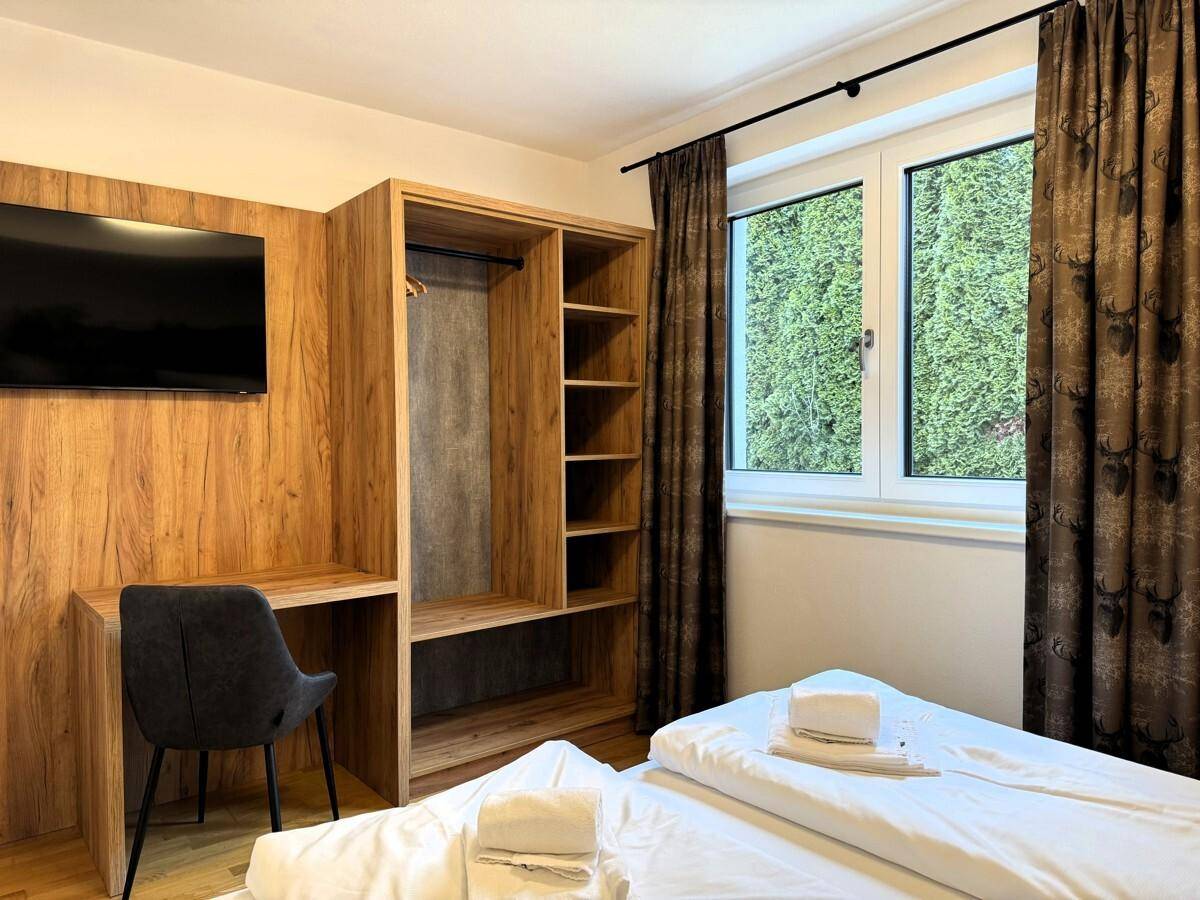 Schlafzimmer mit Doppelbett, offenem Kleiderschrank und integriertem Schreibtischbereich.