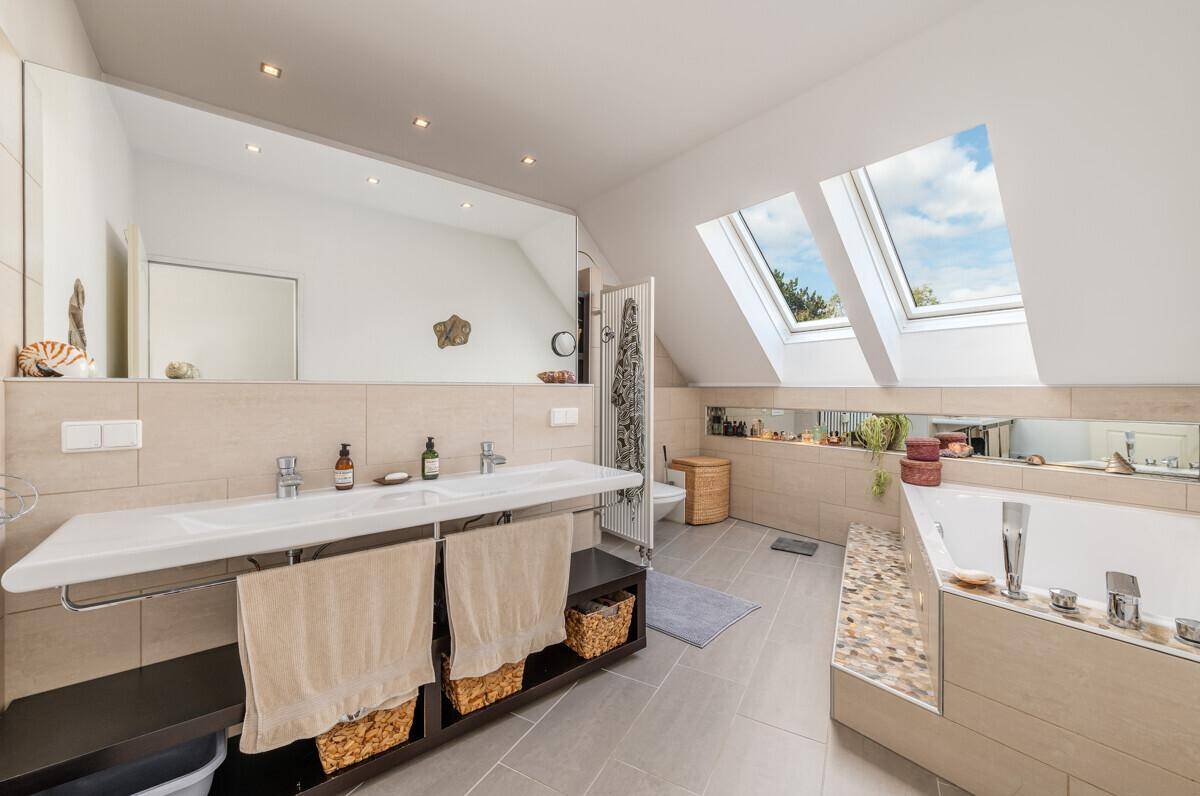 Helles Badezimmer mit Doppelwaschbecken, Badewanne und Dachfenstern für viel Tageslicht.