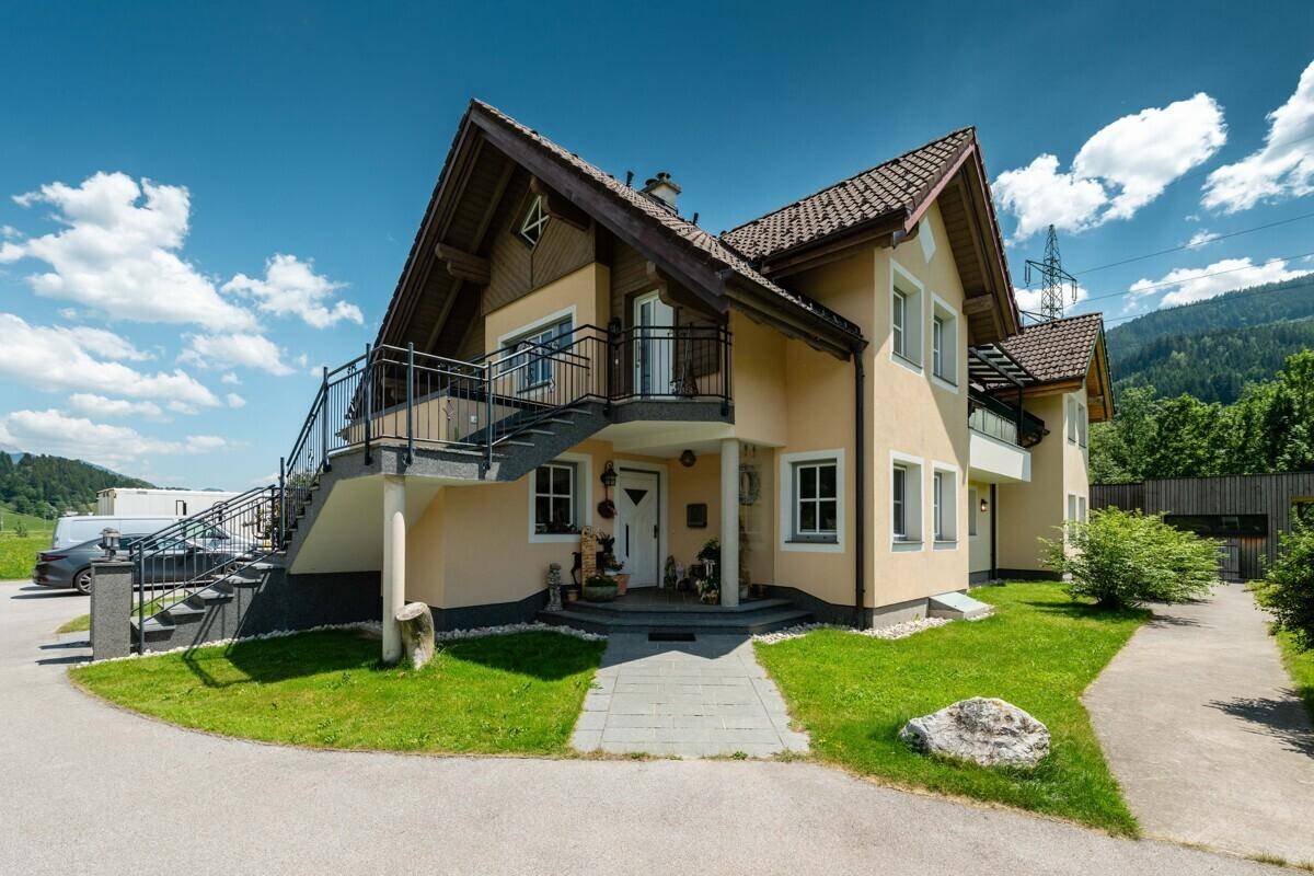 Charmantes Landhaus mit traditioneller Architektur, Balkonen und gepflegtem Vorgarten unter blauem Himmel.
