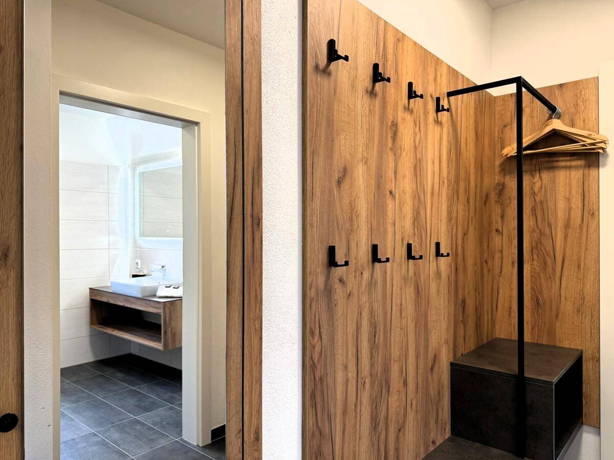 Moderner Garderobenbereich mit Holzwandverkleidung und Haken, angrenzend an ein Badezimmer.