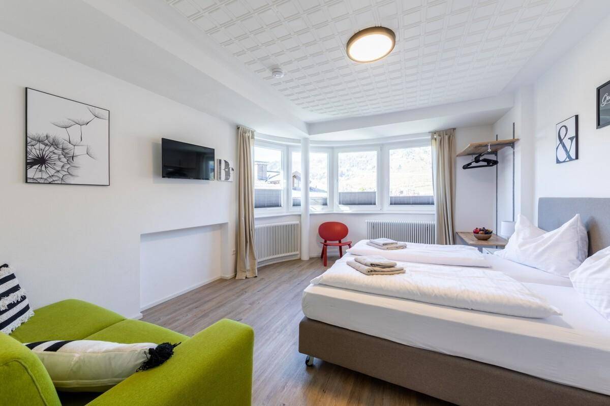 Helles Schlafzimmer mit zwei Einzelbetten, Sofa und großen Fenstern für viel Tageslicht.